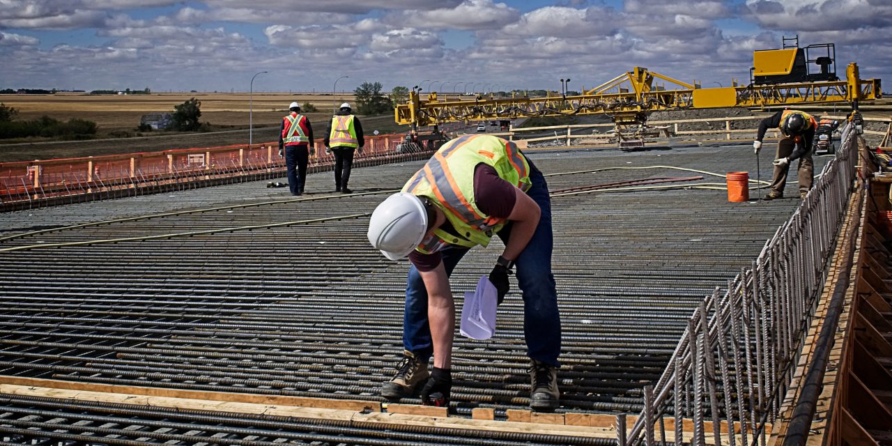 A bridge engineer inspecting spacing diameter and height of steel reinforcing bars with a tape measure on the bridge deck prior to pouring concrete on the reinforced deck supported by steel girders